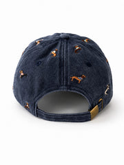Navy denim baseball cap embroidered with colourful dachshund dogs, front view on a white background.