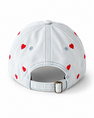 Back view of the light-wash heart-embroidered cap, showing the curved crown and the adjustable strap clipped into its brass buckle.