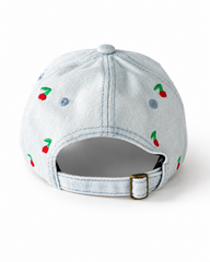 Back view of the light-wash cherry-embroidered cap, showing the curved crown and the adjustable strap clipped into its brass buckle.