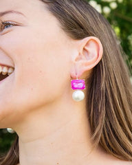 Woman wearing pink and white earrings outdoors with greenery in the background