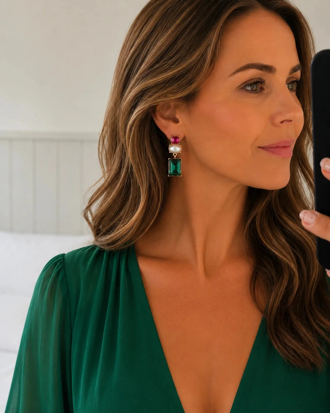 A woman wearing a green gemstone drop earring with a white pearl and pink top stone, shown in a close-up profile shot.
