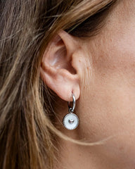 Silver hoop earrings with a white enamel heart charm medallion dangle