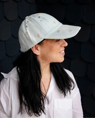 Light-wash denim baseball cap embroidered with pink and yellow flowers, front view on a white background.