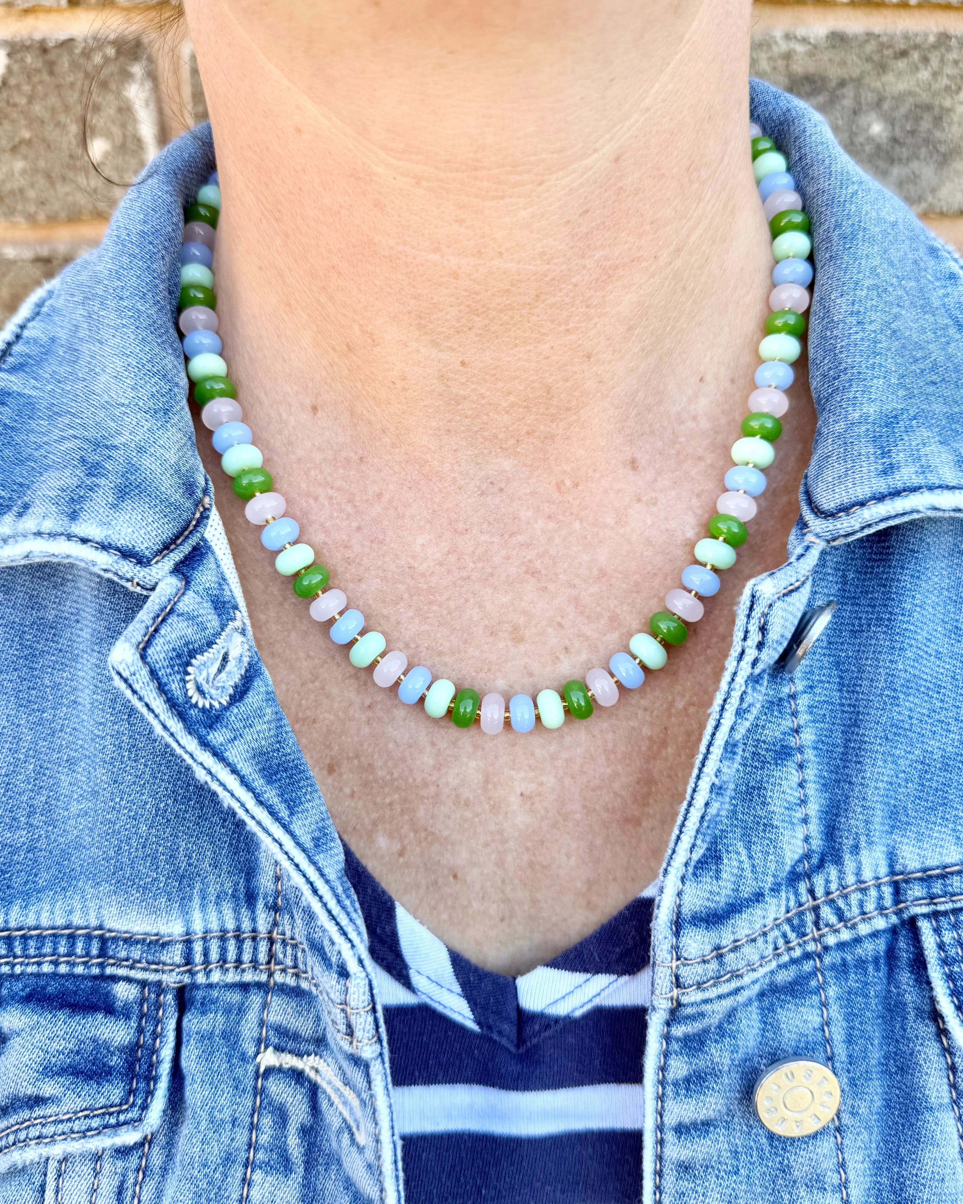 Person wearing a colorful beaded necklace with a denim jacket and striped shirt.