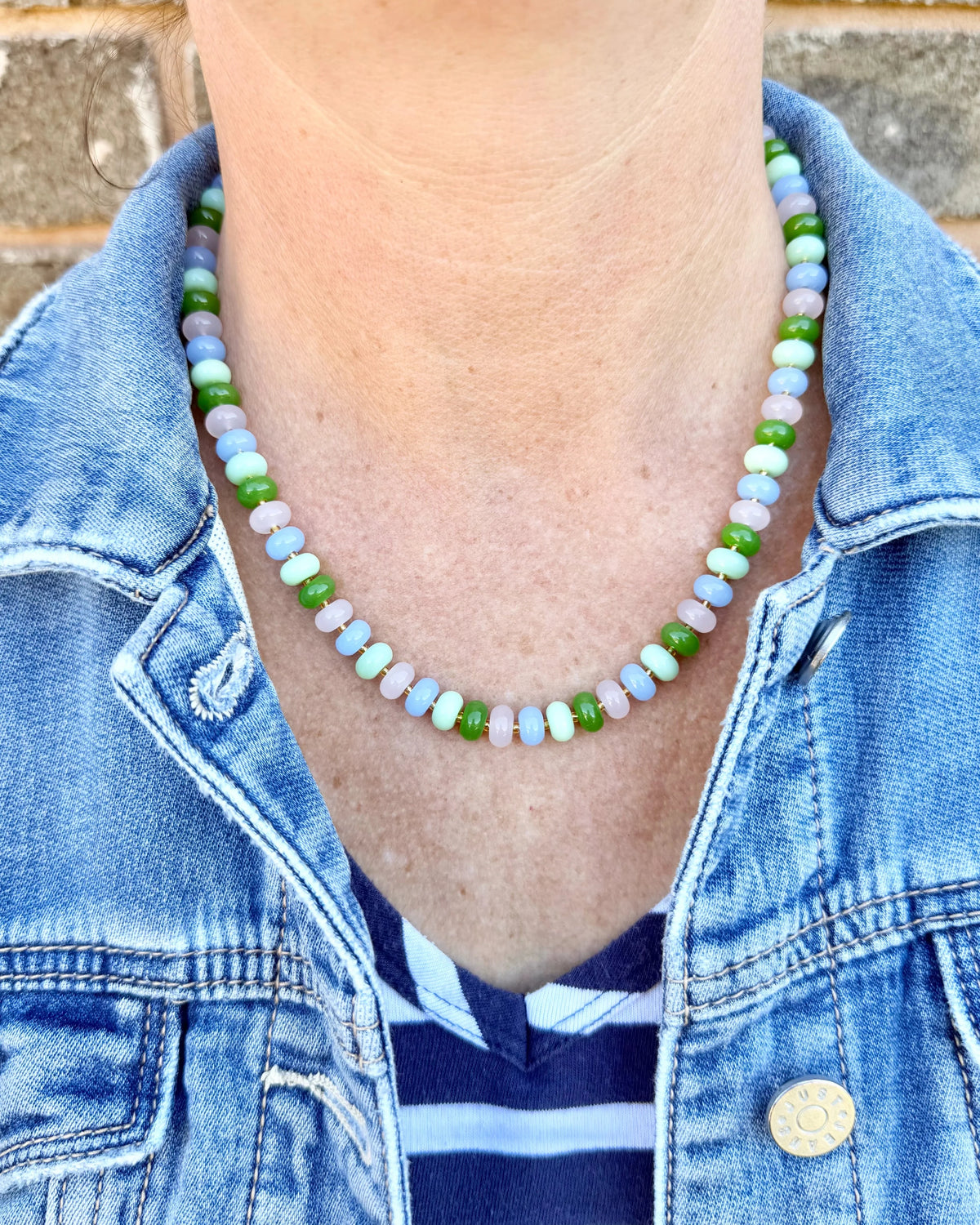 Person wearing a colorful beaded necklace with a denim jacket and striped shirt.
