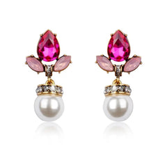 A pair of gold-colored earrings with pink crystal accents and faux pearl drops.