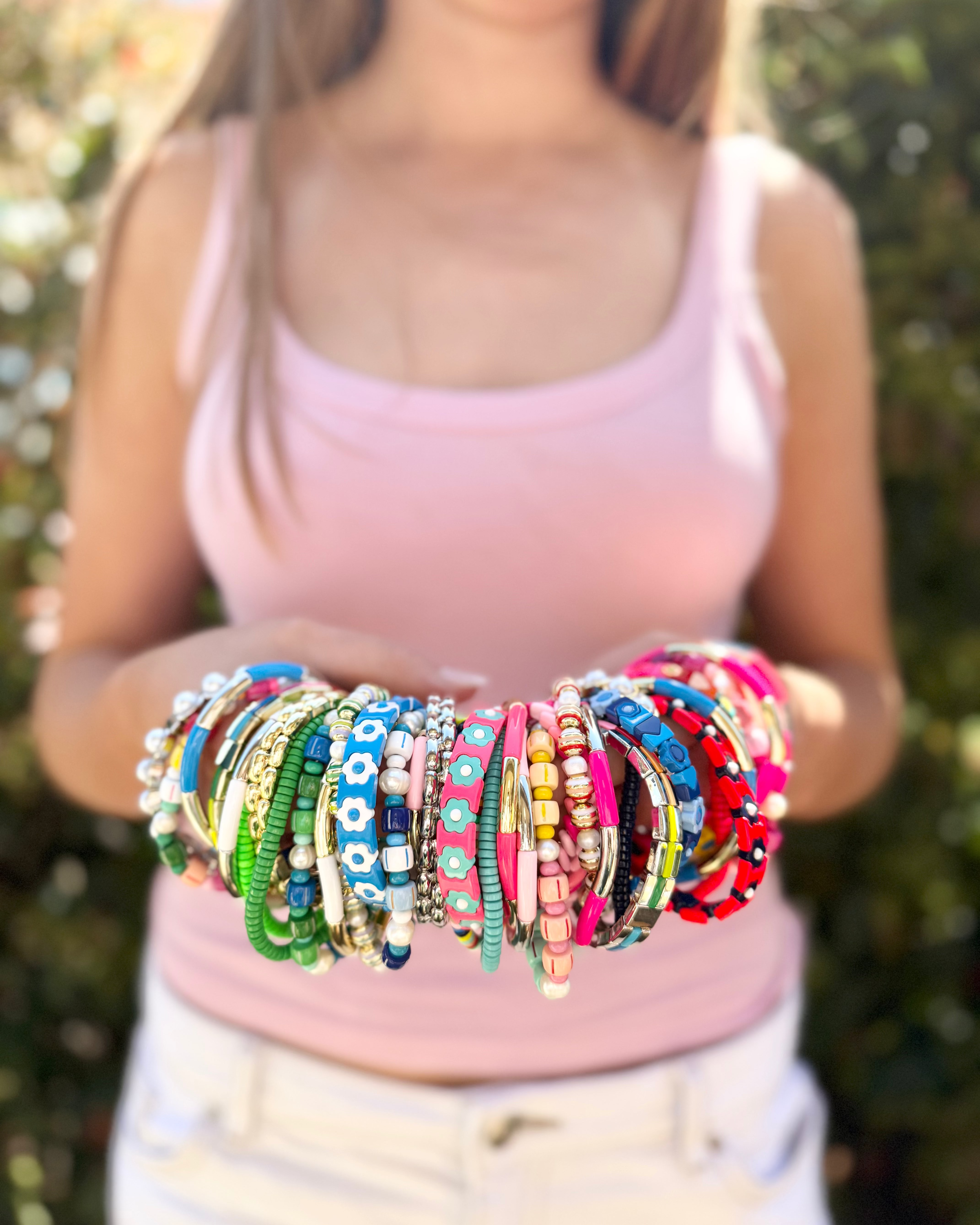 Person holding a collection of colorful bracelets against a blurred natural background