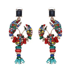 Colourful lobster statement earrings with multicolour crystals worn by woman in red dress at outdoor lunch