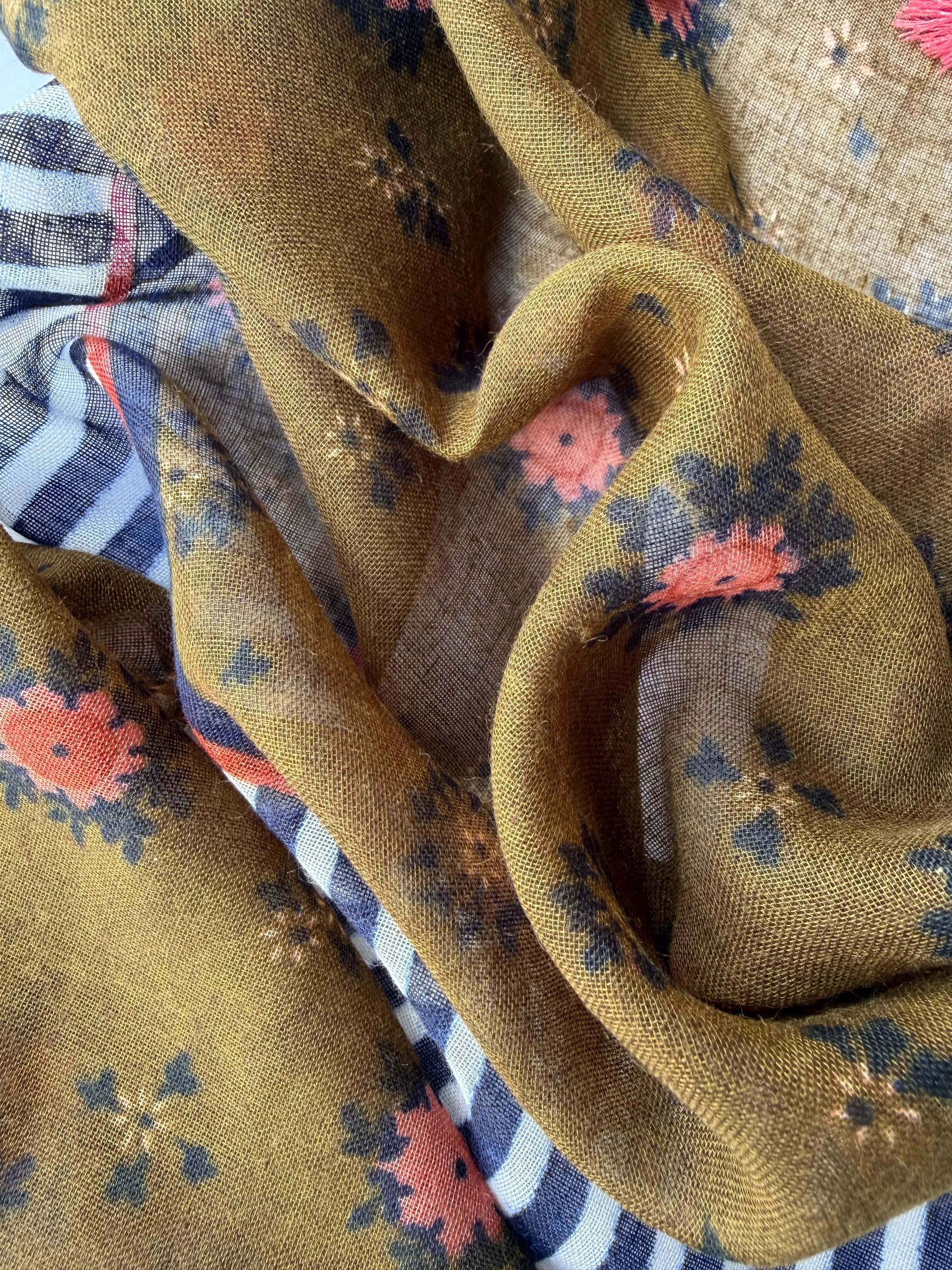 Lightweight scarf with a coral floral print on olive green, a border of rust, navy and navy and white stripes, and coral and tan tassels