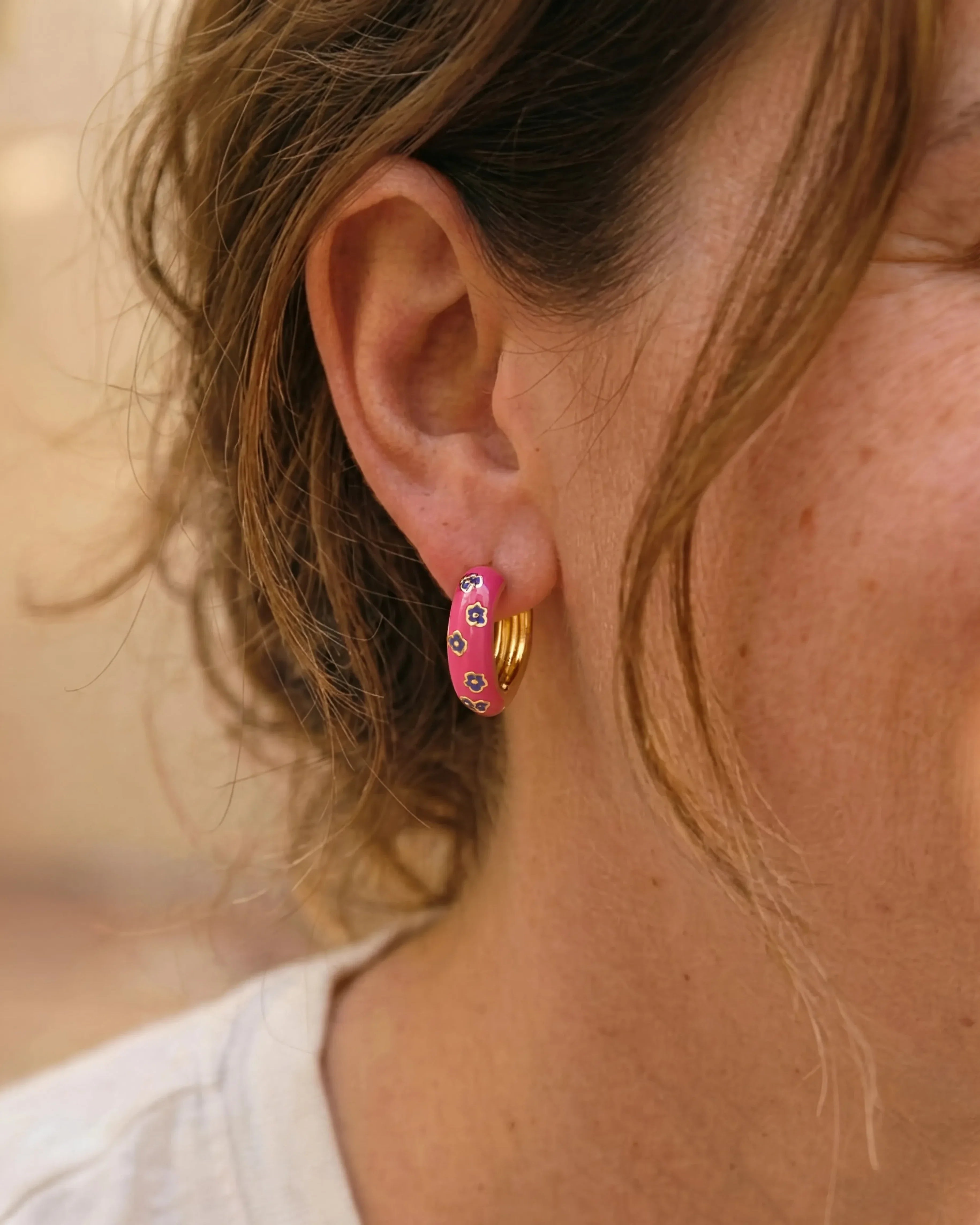 Woman wearing pink enamel gold hoop earrings with purple flower pattern