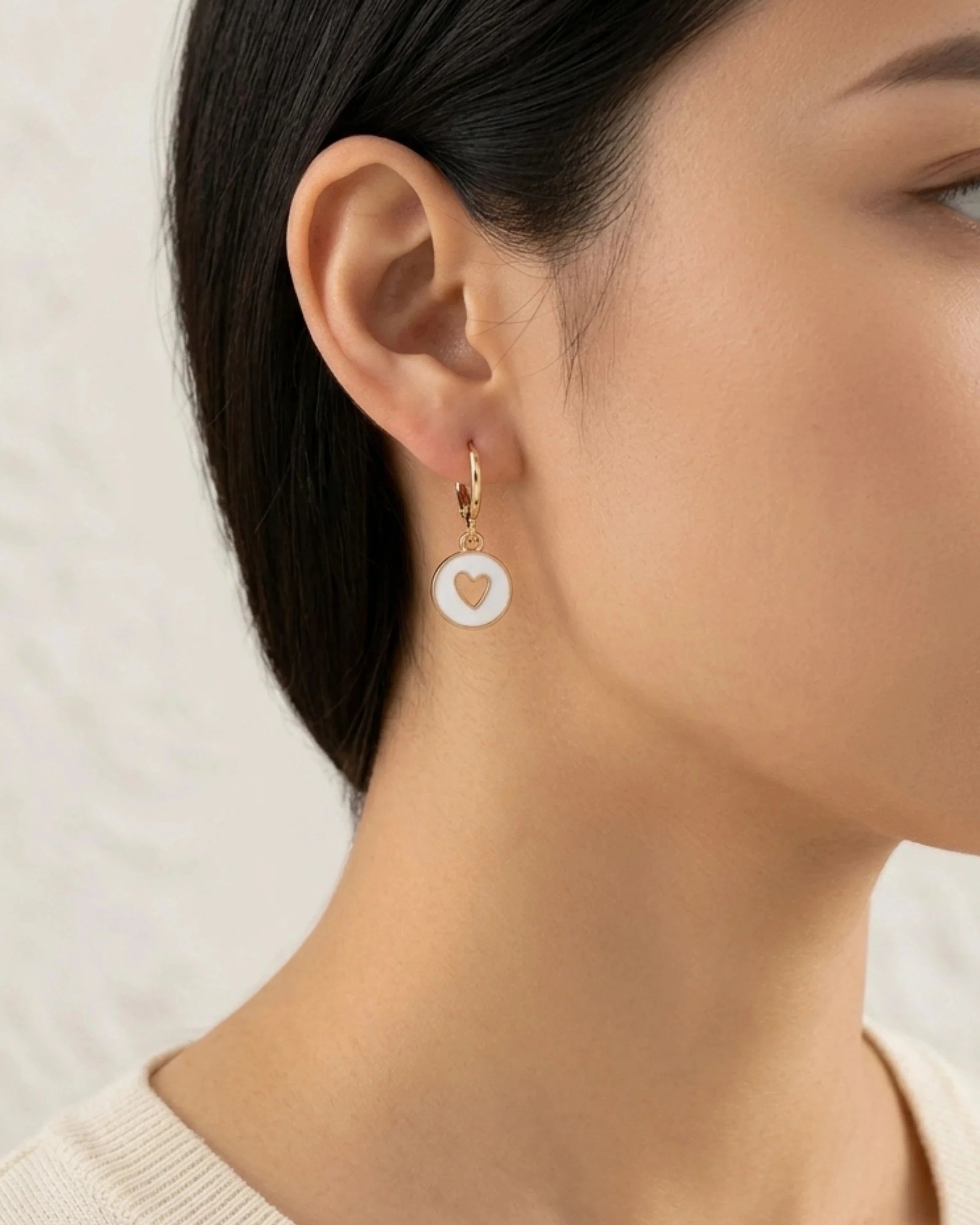 Woman wearing white enamel gold hoop earring with heart cutout detail