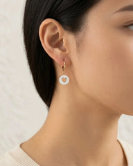 Woman wearing white enamel gold hoop earring with heart cutout detail
