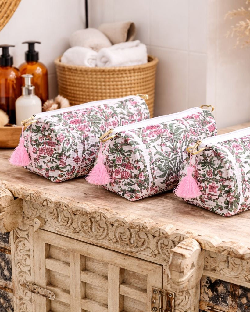 Three floral-patterned cosmetic bags with pink tassels on a wooden surface.