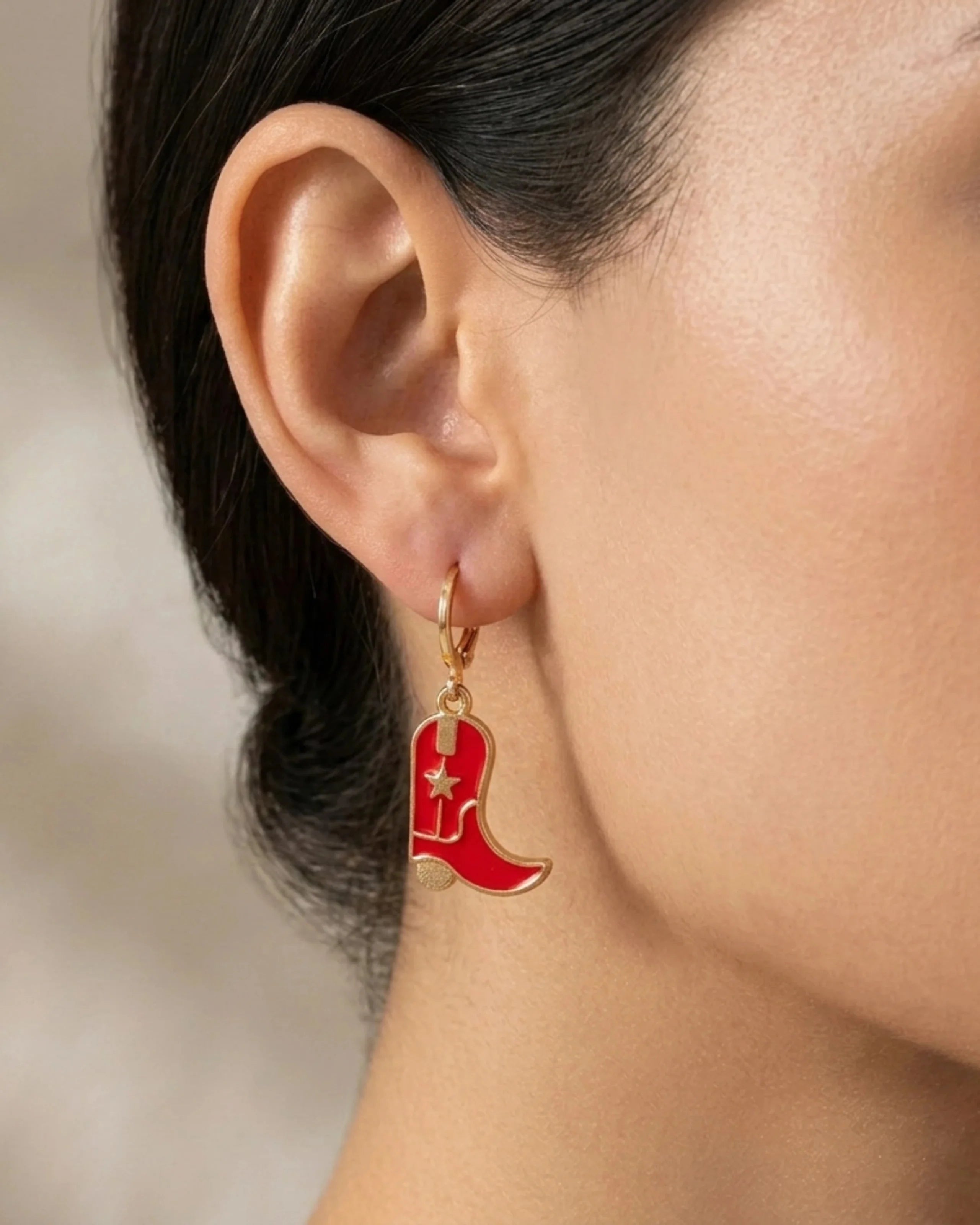 Woman wearing red enamel cowboy boot dangle earrings with gold hoop