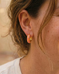 Woman wearing Jane orange enamel chunky hoop earrings with pink flower detail by Greenwood Designs, styled with a white top outdoors